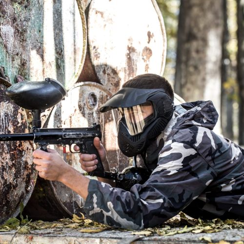 A man with a gun in a uniform and a mask on his face, playing paintball . Sports active games in the fresh air.