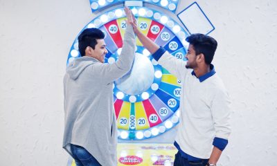 We are millionaires! Very excited two young asian guys against fortune wheel win at lottery big prize. Give high five each other.